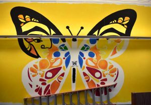 Art as protest: The sign posted on the butterfly currently being painted on the Gallegly Center soundproof wall in the Pearson Library reads “migration is beautiful” in tribute to students in the DACA program. Photo by Natalie Elliott- Photojournalist