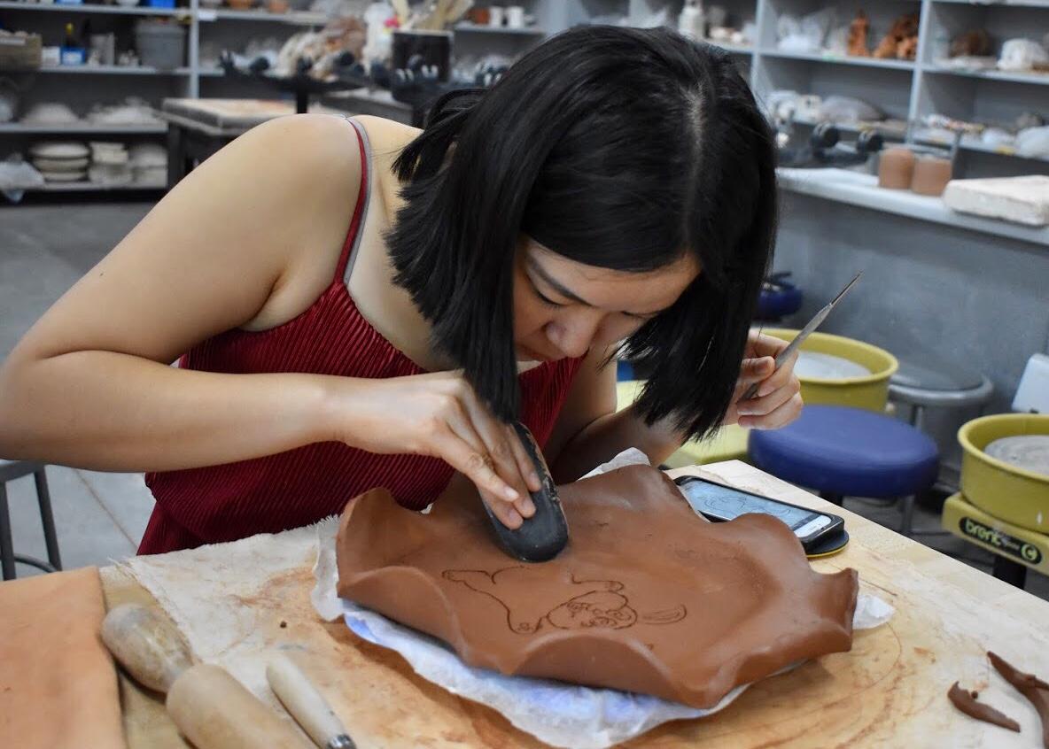 Graduate student Chicha Tansiri designs in an image of a bunny on her red clay pottery plate. Photo by Aliyah Navarro- Photojournalist.