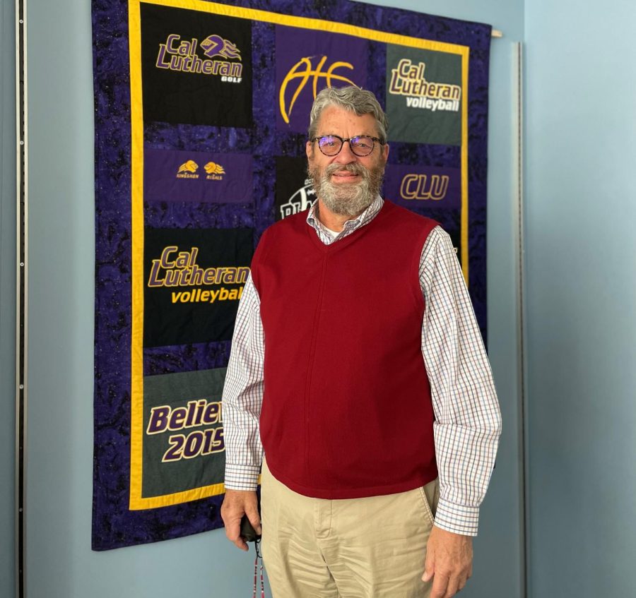 Interim Dean of the College of Arts and Sciences Timothy Hengst standing in front of a blanket made by his wife in his office.