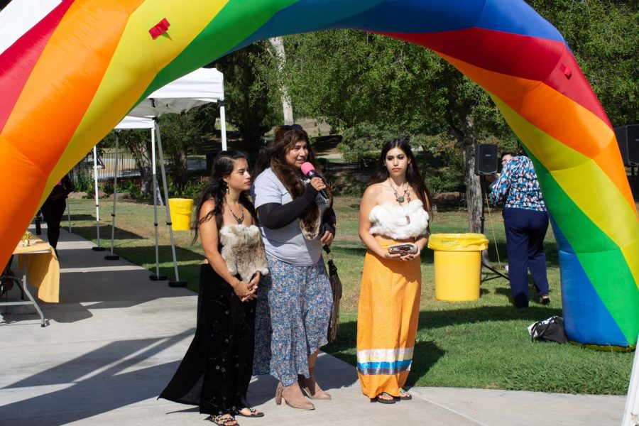 Three+women+standing+underneath+an+inflatable+rainbow+bridge%2C+speaking+about+Indigenous+Peoples+Day.