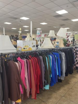 thrift store rack with colored shirts and and lamp shades on shelf above
