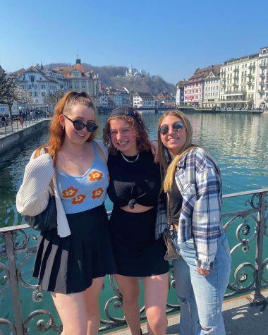 Sophia Davies y dos amigas posando en un puente con vistas a un río y edificios a ambos lados en España.
