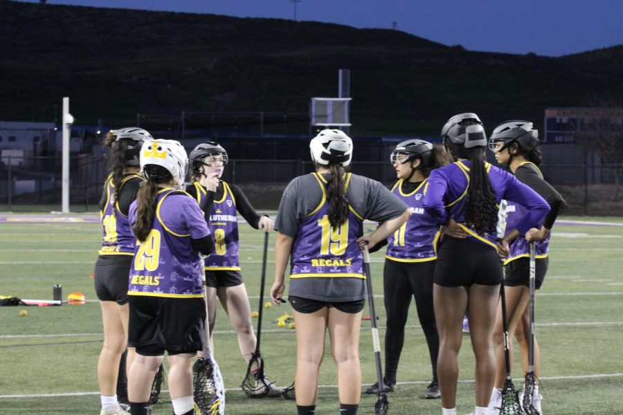 Members of the Regals lacrosse team huddle around in a circle during a practice session.